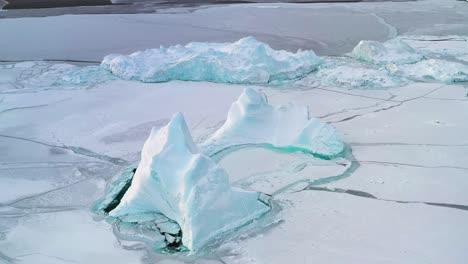 Aerial-view-tilting-away-from-icebergs-in-middle-of-icy-sea,-in-Ilulissat,-Greenland