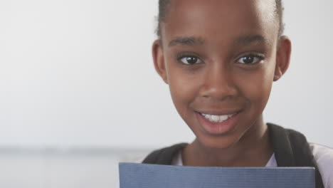 smiling african american girl holding notebook and wearing backpack, ready for school
