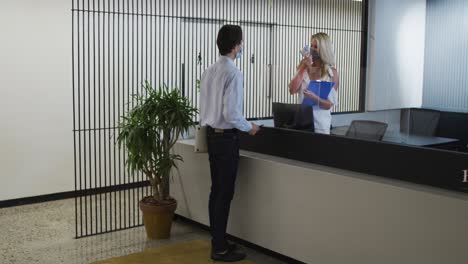 caucasian businesswoman wearing face mask checking coworkers temperature