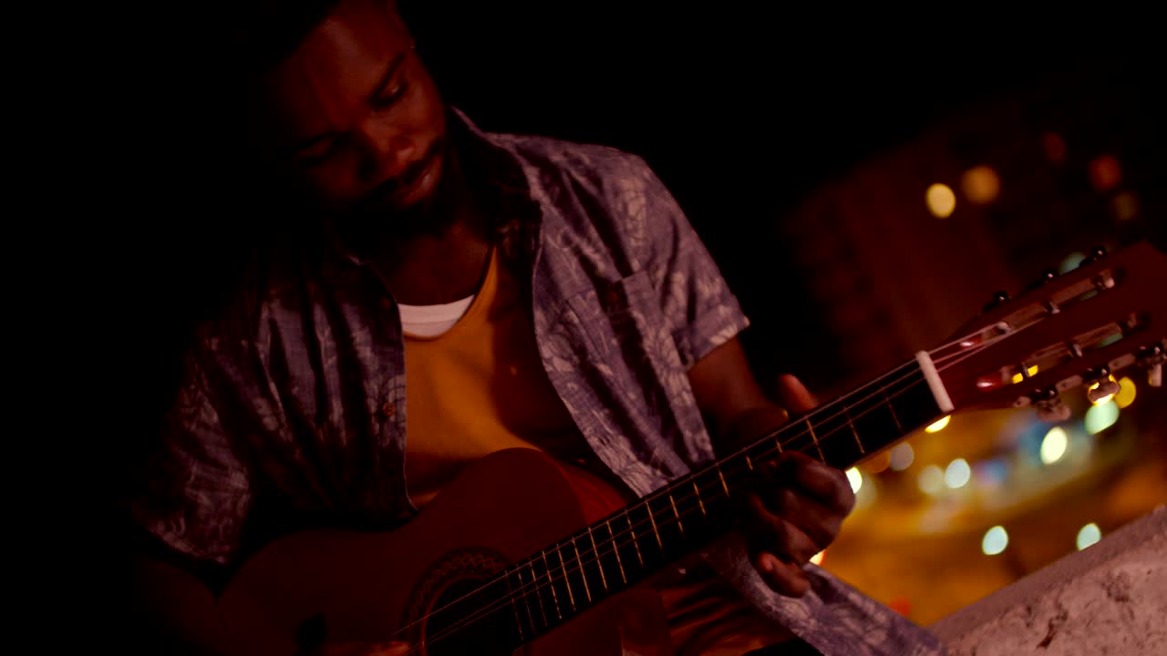 Giovane uomo afroamericano hipster che suona la chitarra di notte.