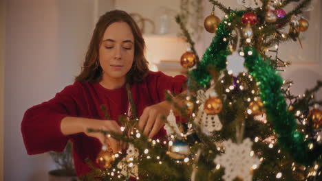 mujer atando adornos de navidad en el árbol