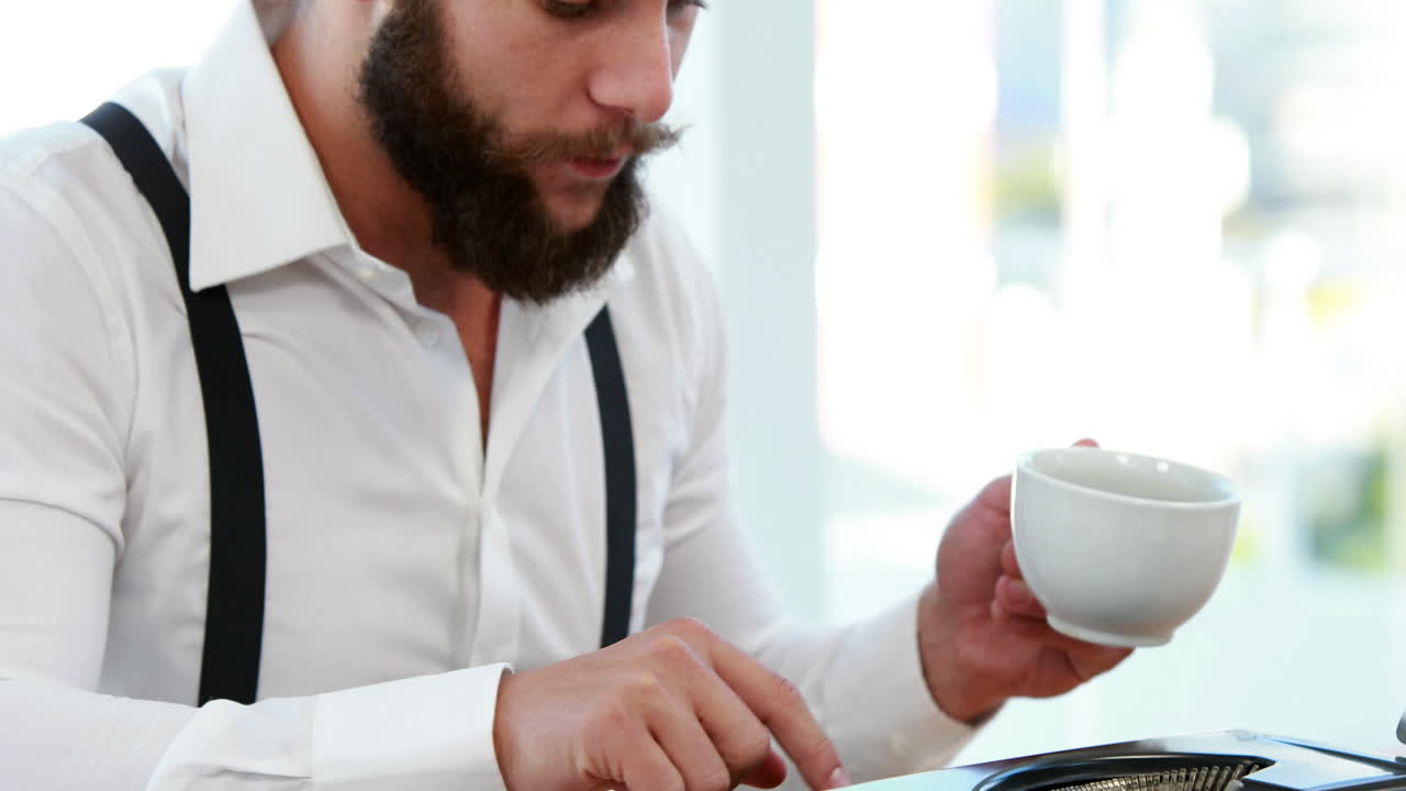 Uomo d'affari informale che utilizza una macchina da scrivere e beve caffè