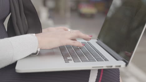 primer plano de una mujer sentada afuera escribiendo, trabajando en su computadora portátil mientras la gente pasa caminando - sin calificar