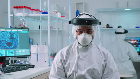 doctor man looking at camera sitting in lab dressed in ppe suit