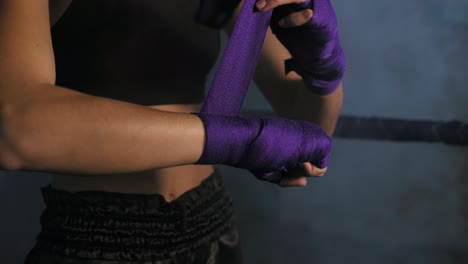 Closeup-view-of-female-hands-being-wrapped-for-boxing-in-dark-room-with-smoke.-Young-fit-woman-wrapping-hands-with-purple-boxing-bandage.-Shot-in-4k