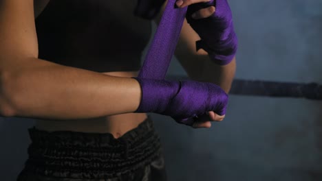 closeup view of female hands being wrapped for boxing in dark room with smoke. young fit woman wrapping hands with purple boxing bandage. shot in 4k