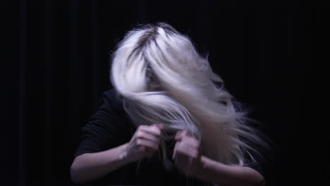 blond woman banging her fists on desk in anger, shaking her head in stress in a dimly-lit room illuminated by a single overhead light