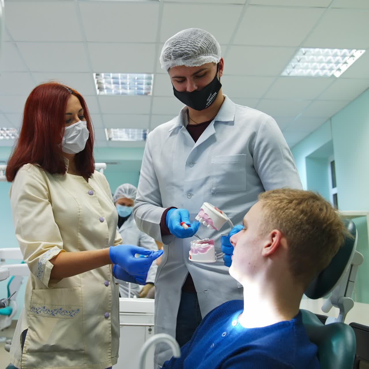 Tall male medic student shows the patient teeth model. Future dentist teaching a patient to clean teeth correctly