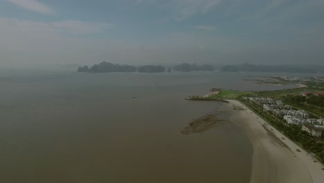 Aaerial-view-of-a-beach-with-Halong-Bay-in-the-background,-Vietnam