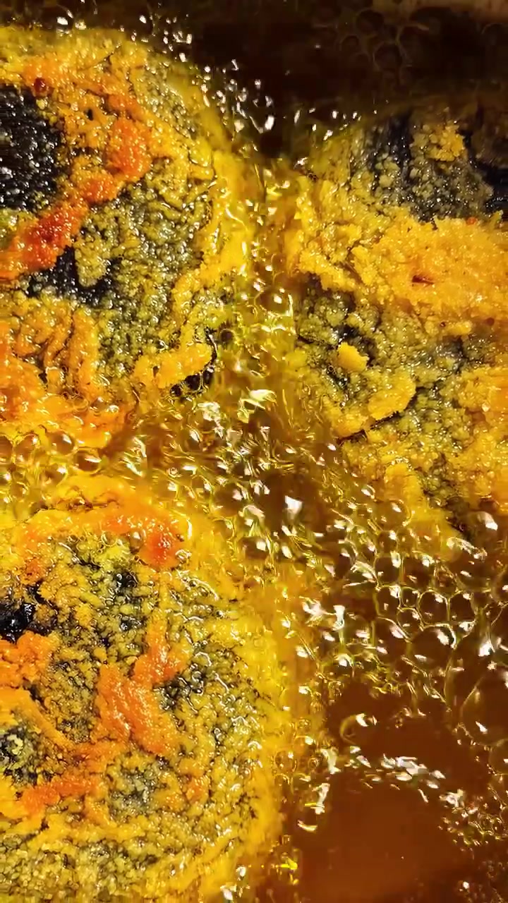 Crumbled dark meat sizzles in hot bubbling oil from above, dark crispy edges forming against golden fat, capturing the intensity of deep frying. Top down close up detail