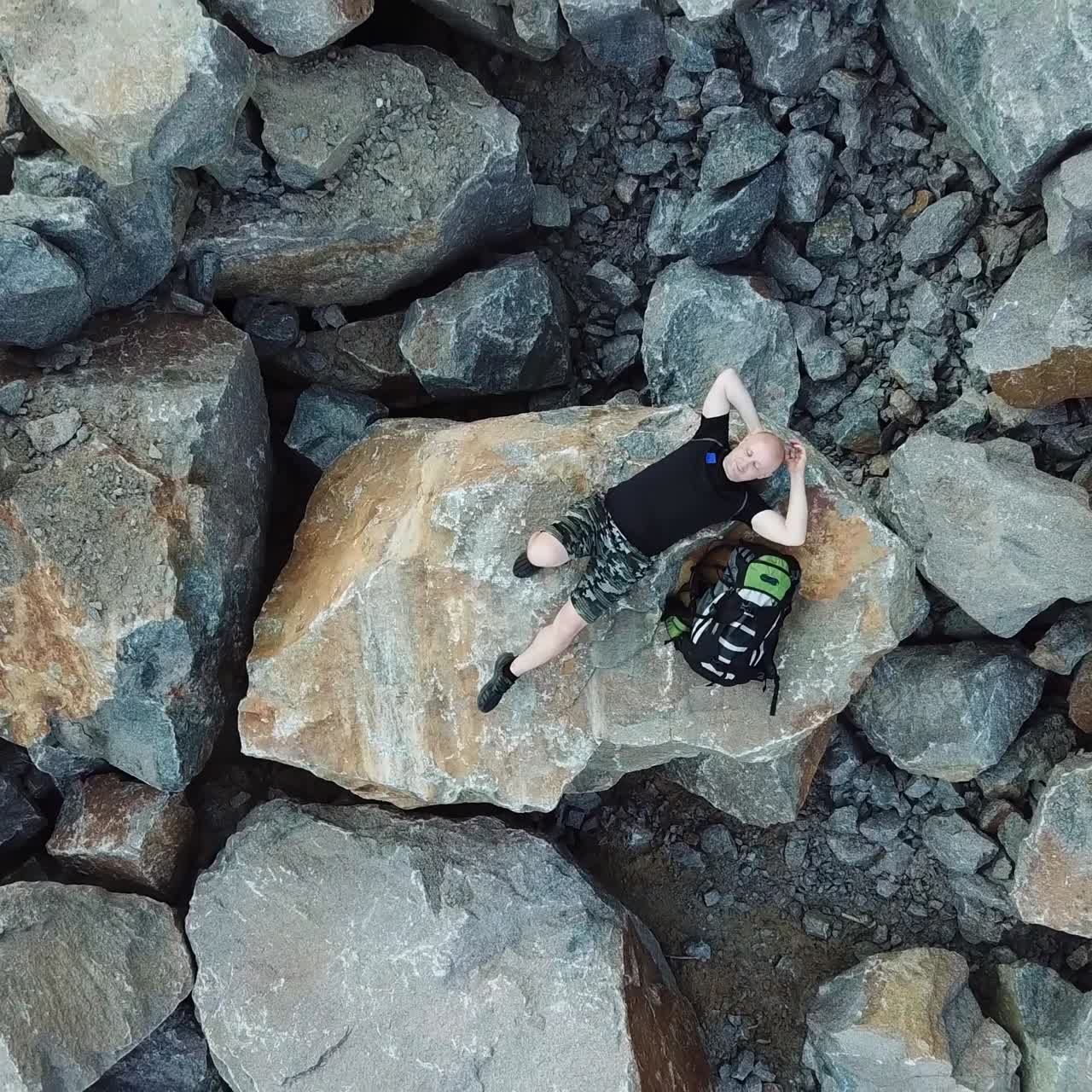 Bald Man lays on a large stone. Tourist with a backpack in shorts and t-shirt is resting. Aerial view