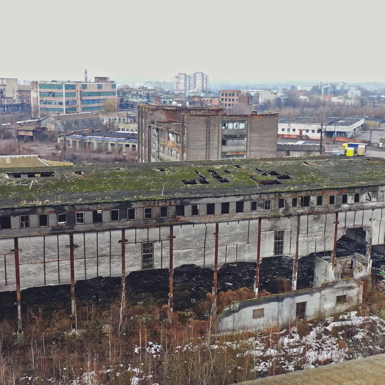 Almost destroyed building with holey roof in the city. Top view of ruined industrial building and some cars on a road. Aerial view