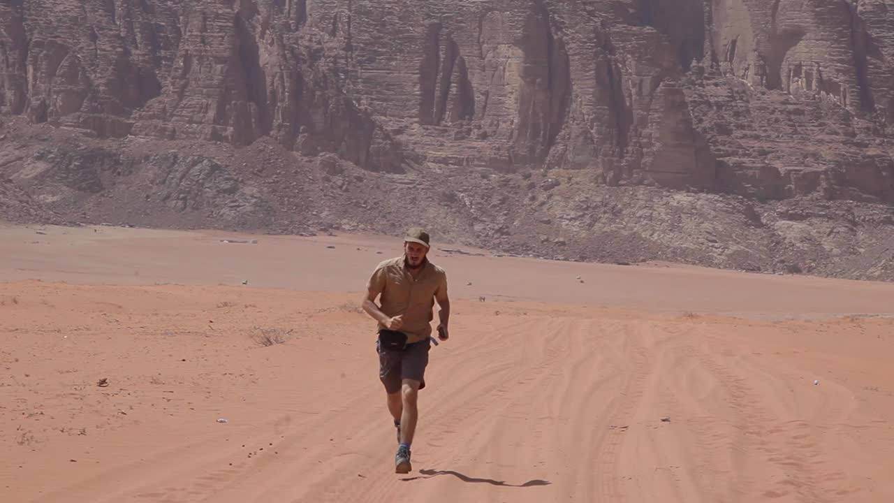 aventurero corriendo por el árido desierto, montañas al fondo, wadi rum, jordania, tiro estático