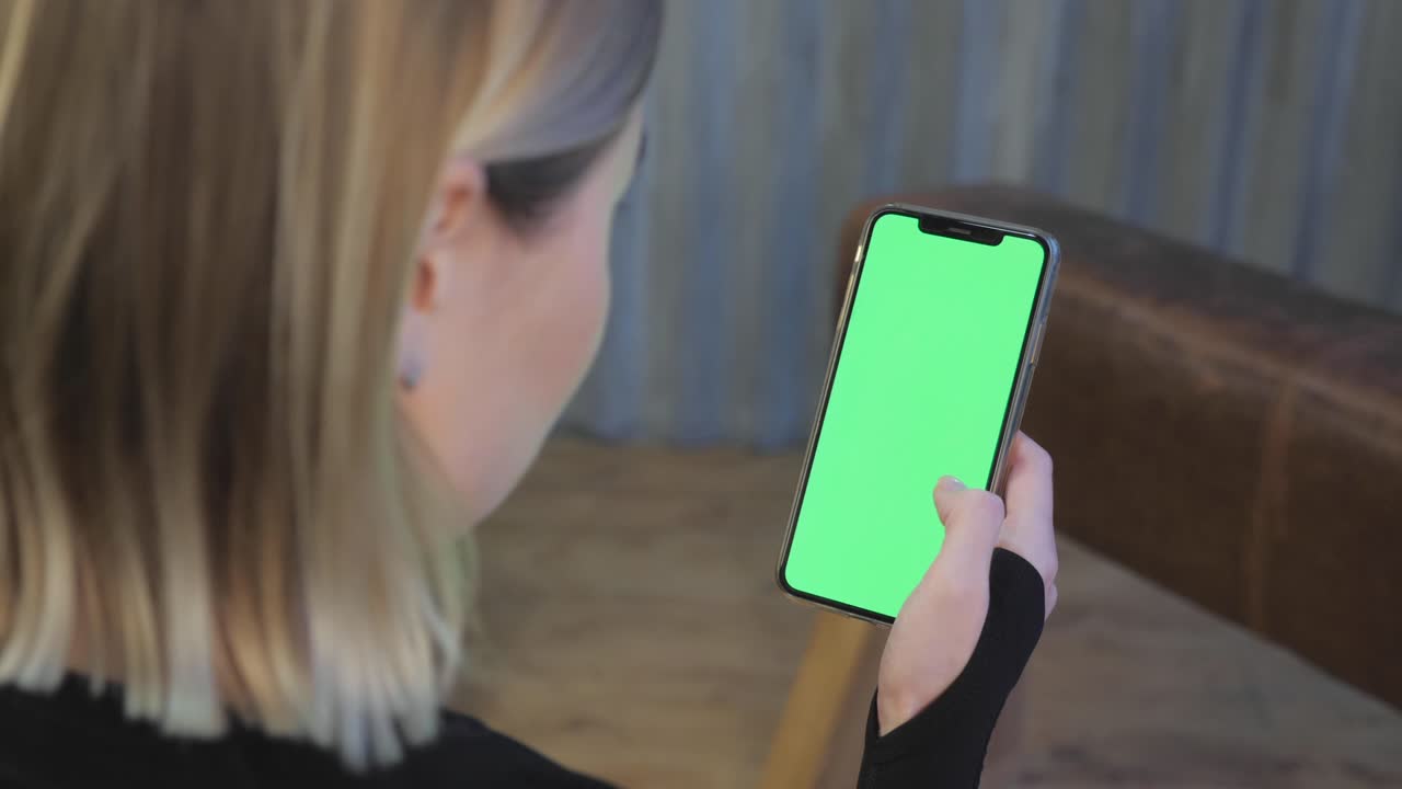 젊은 운동선수 여성이 손에 스마트폰을 들고 녹색 크로마키 화면을 보여주고 스포츠 앱을 보고 체육관에 있습니다.