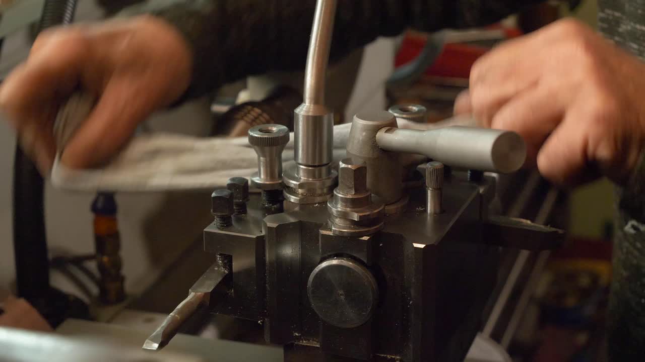 Operaio metalmeccanico caucasico che pulisce una parte di un tornio con un panno, dettaglio delle mani e dell'officina