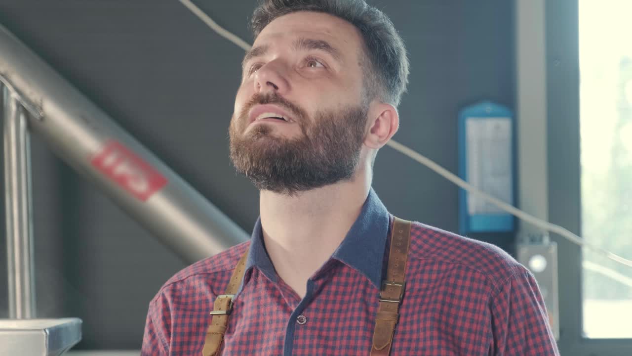 un joven cervecero con un delantal de cuero controla la molienda de semillas de malta en un molino en una cervecería moderna