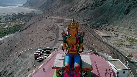 tall budha structure made of gold standing in the middle of a mountain valley