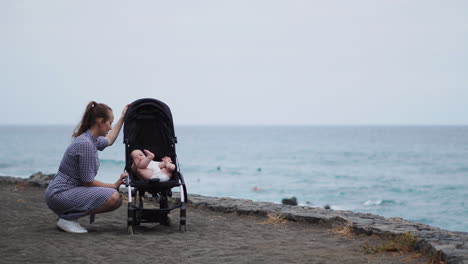 amid the ocean's tranquil setting, a young mother's interactions with her baby in the stroller highlight her affectionate and nurturing role within this sweet family