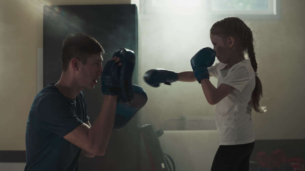 Kid punches glove pads exercising with trainer in gym. Martial arts instructor teaches little girl to attack in sports school slow motion. Healthy child