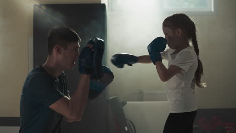 kid punches glove pads exercising with trainer in gym. martial arts instructor teaches little girl to attack in sports school slow motion. healthy child