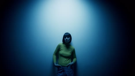 mujer con suéter amarillo contra la pared iluminada de azul