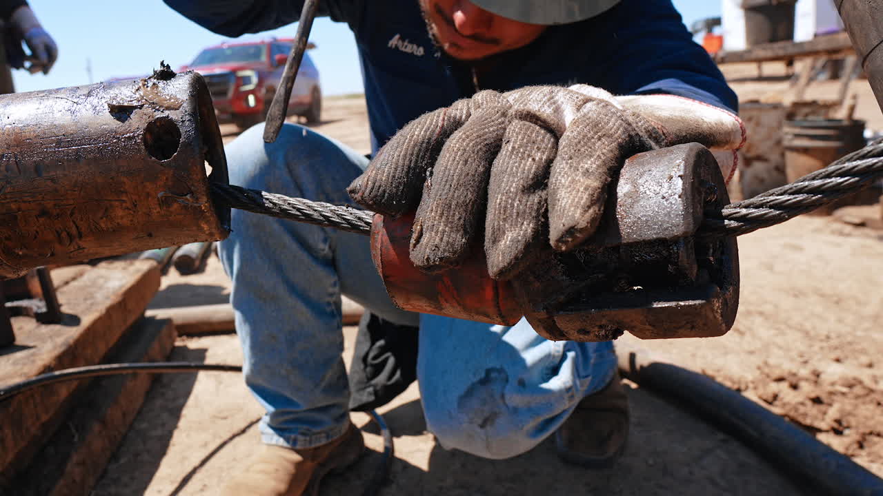 Worker wearing gloves smudged with oil tar holding the wire with metal detail on it. Man uses screw driver in the pipe. Site for oil production. Close up.