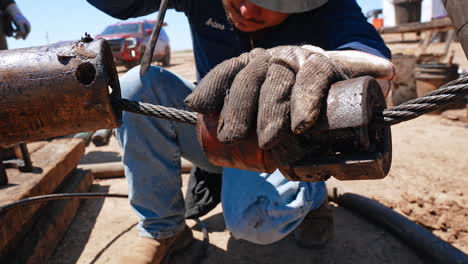 worker wearing gloves smudged with oil tar holding the wire with metal detail on it. man uses screw driver in the pipe. site for oil production. close up.
