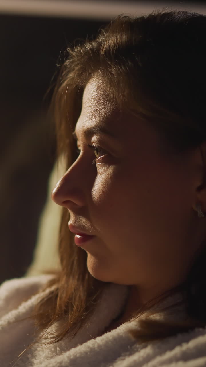 Lady suffers from depressive thoughts relaxing in dimly lit hotel room. Woman immersed in thoughts gazes at wide window. Video depicts concept of loneliness