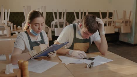 Two waiters, owners of a restaurant, are depressed and frustrated sitting at a table counting costs and lost money due to the pandemic crisis