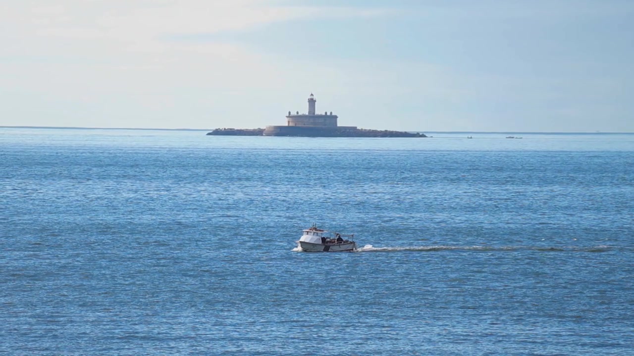 Portekiz'de puslu bir gökyüzü altında uzak bir adada tarihi Bugio Deniz Feneri'nin göründüğü, Tagus Nehri haliçinin sakin mavi sularında seyreden küçük bir balıkçı teknesi.
