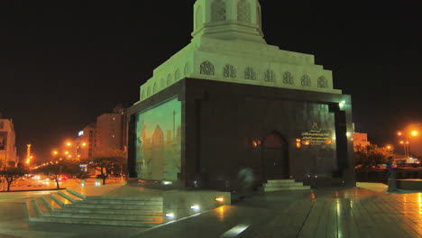 night scene in muscat with traditional monument lit up surrounded by city lights and a few pedestrians