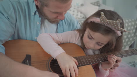 little daughter dressed as a princess plays guitar with her daddy at home