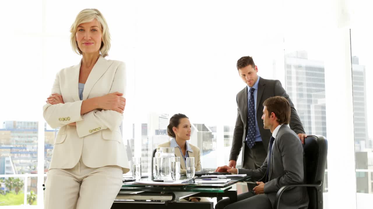 mujer de negocios apoyada en el escritorio con el equipo detrás de ella