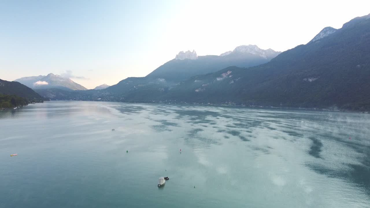 Morning mist over the water on Lake Annecy. Drone footage raises and moves forward capturing this spectacular view