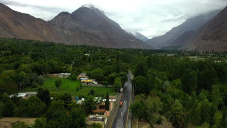 dramatic drone shot following a tuk-tuk on the karakoram highway pakistan in a small town or village, wide chasing aerial shot