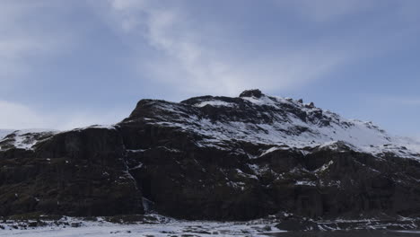 establishing aerial shot of a large snowy mountain with a frozen lake below in iceland