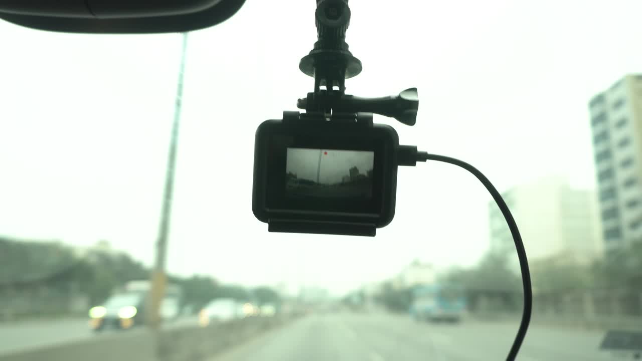 close-up of a dashcam hanging on the windshield of a car recording the route of the trip through the highway out of focus in the daytime in 4k