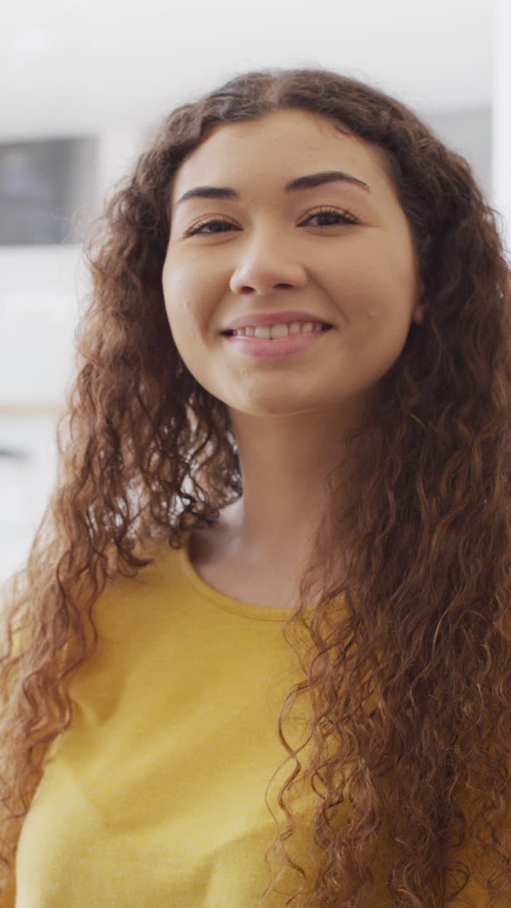 retrato de video vertical de una mujer biracial con cabello largo sonriendo a la cámara en el interior