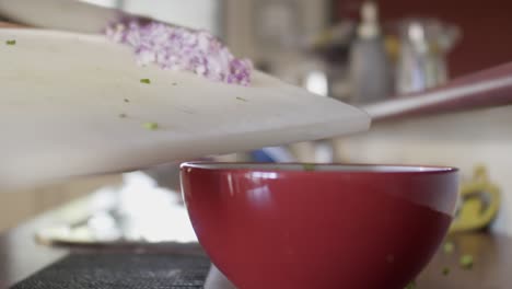 A-chef-scraping-sliced-Spanish-onion-into-a-red-mixing-bowl