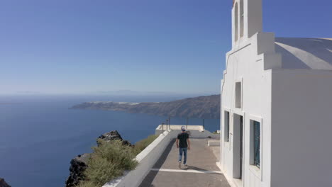 aerial: one man walks next to a church in santorini, greece on a sunny day