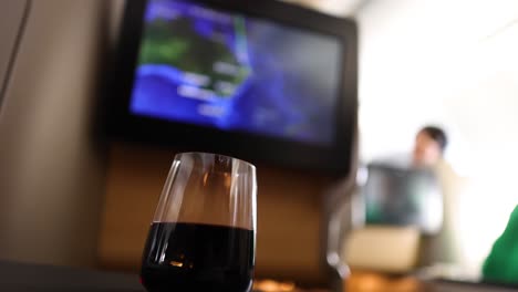 passenger enjoys wine, watching screen on airplane