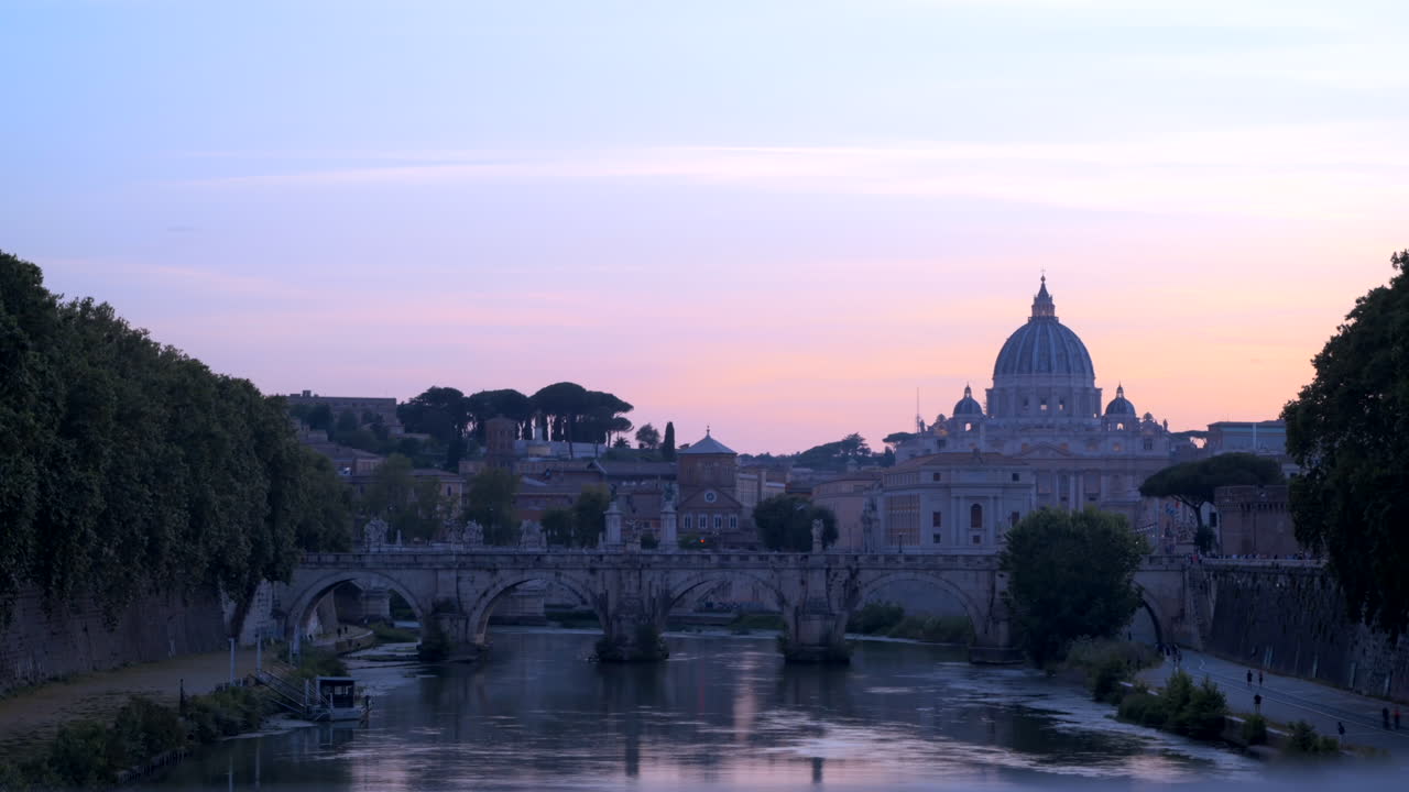 Rome, Italy - August 16, 2024: St. Angelo Bridge across River Tiber with the St. Peter's Basilica on the background at sunset