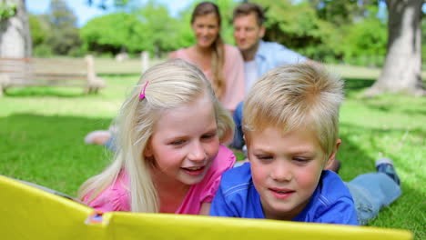 brother and sister reading a book together while lying in the grass