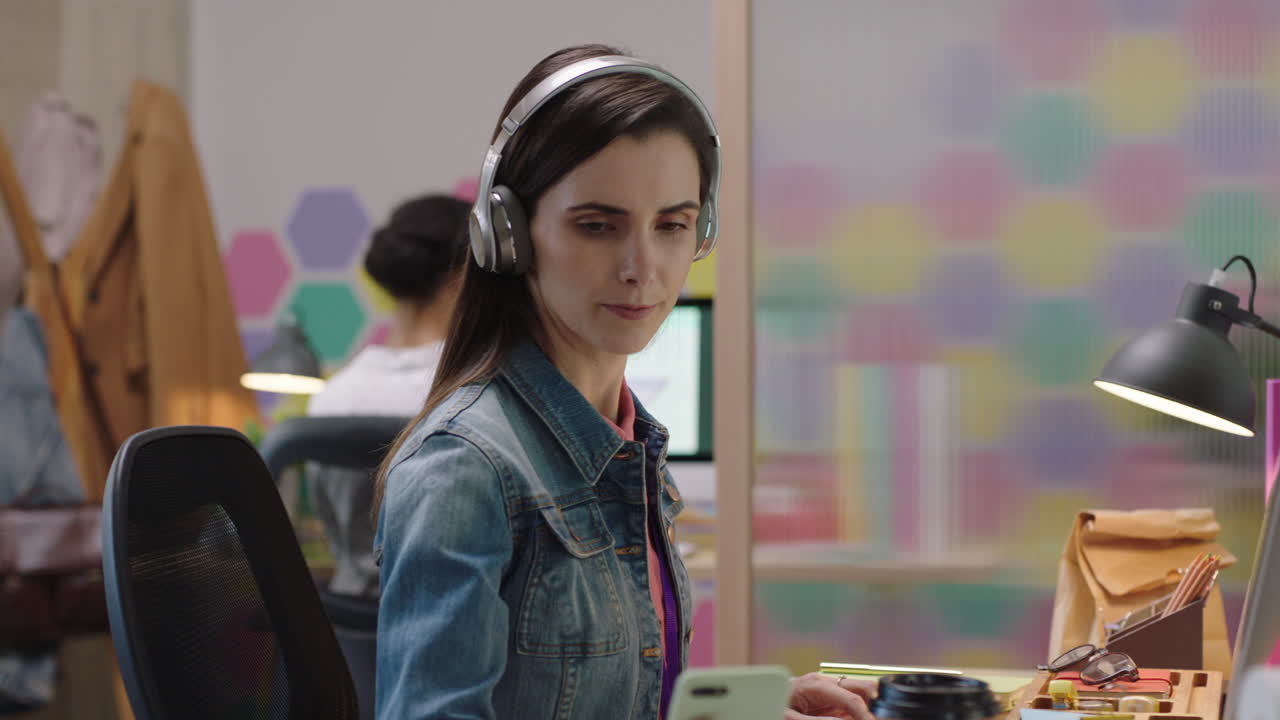 mujer de negocios joven usando la computadora navegando en línea trabajando en un proyecto de red escuchando música disfrutando de la oficina de inicio de moda comprobando el teléfono inteligente