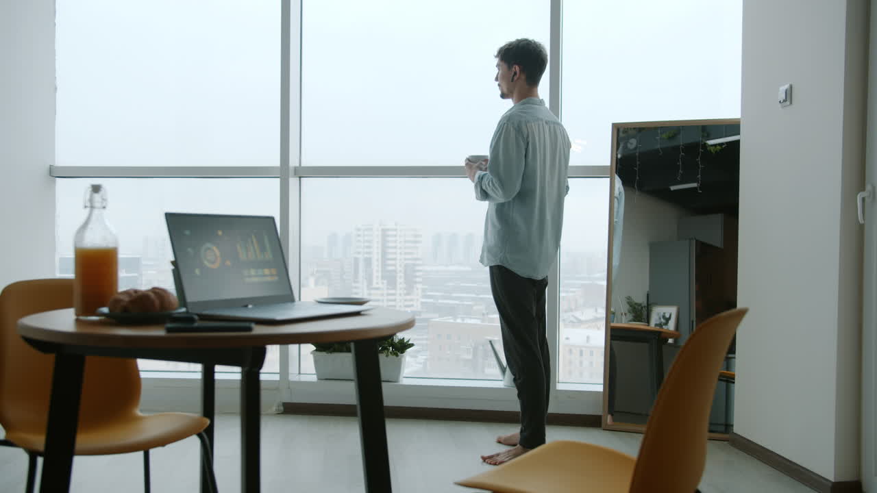 Homem desfrutando de uma pausa para o café com vista para a cidade do seu apartamento moderno