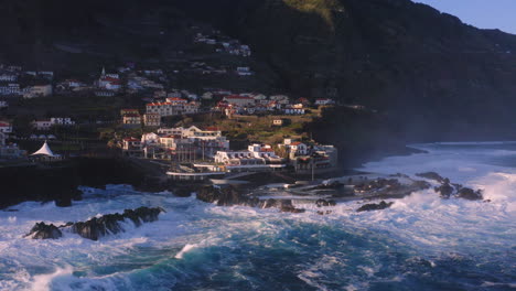 epic aerial shot of port moniz village with crashing waves against rocks during sunset