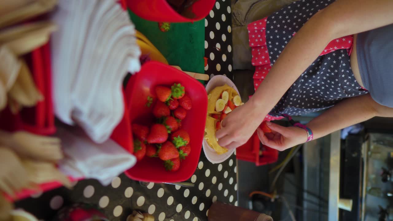 mujer atractiva vestida con ropa vintage cortando fresas preparando gofres con cubiertos de jarabe de plátano y chocolate y servilletas listas en la mesa en el festival de jazz de música de verano video vertical