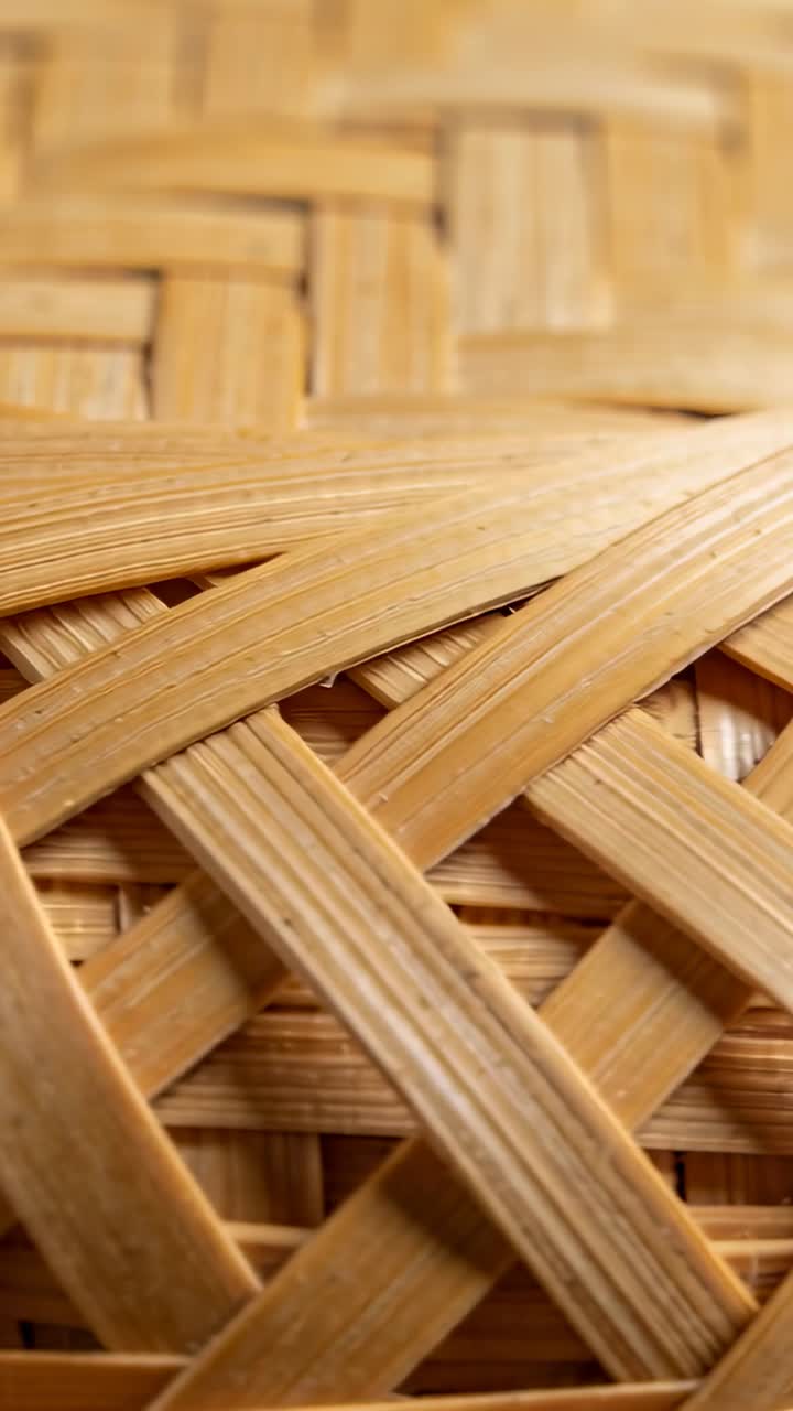 Video verticale: Telecamera che si sposta mettendo a fuoco un pannello in rattan intrecciato in primo piano, rivelando la venatura del legno