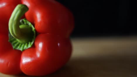 Rote-Paprika-Rollt-Auf-Holzschneidebrett-Auf-Schwarzem-Hintergrund,-Zeitlupe