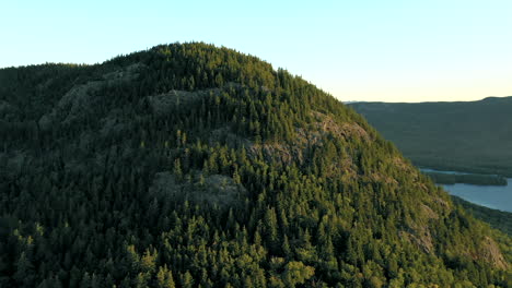 Aerial-drone-shot-orbiting-around-the-peak-of-Bore-Mountain-above-the-thick-green-forest-trees-and-lakes-of-the-Maine-wilderness